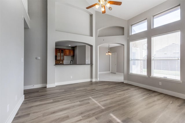 318 Mesquite Ct, Murphy, TX 75094 - unfurnished living room featuring a ceiling fan, arched walkways, light wood-style flooring, a chandelier, and high vaulted ceiling