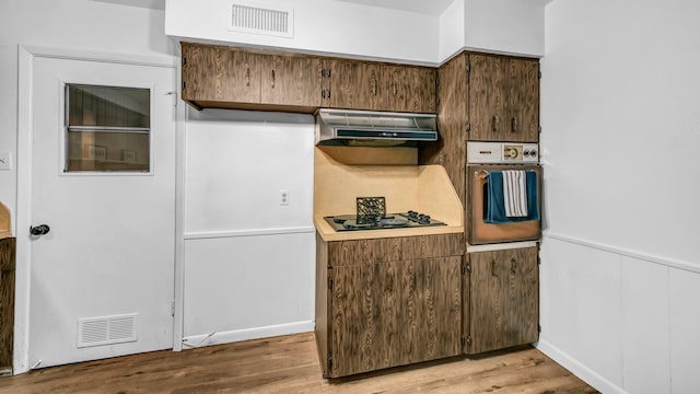100 Oakhurst Dr, Hurst, TX 76053 - kitchen with oven, black gas cooktop, exhaust hood, wainscoting, and light wood finished floors