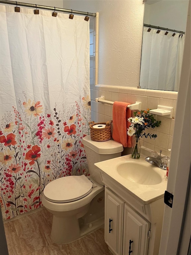 100 Oakhurst Dr, Hurst, TX 76053 - full bath featuring tile walls, wood finished floors, toilet, vanity, and a wainscoted wall