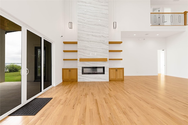 733 El Barco, Corsicana, TX 75109 - unfurnished living room with light wood-type flooring, a towering ceiling, a large fireplace, and baseboards