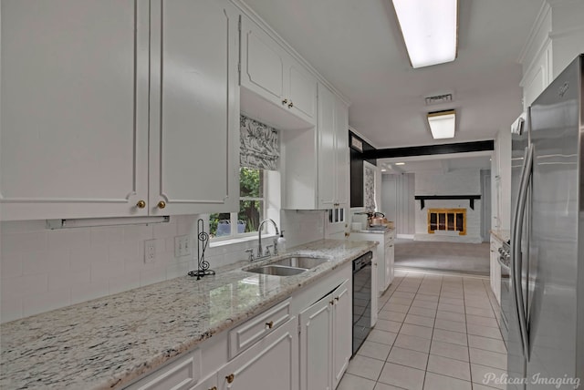 kitchen with freestanding refrigerator, black dishwasher, a sink, a brick fireplace, and white cabinetry