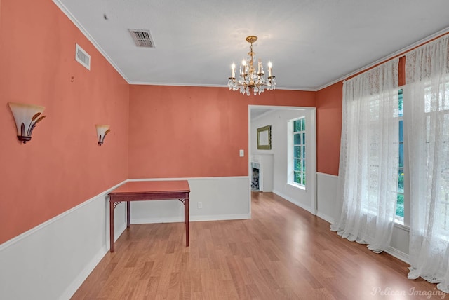 unfurnished dining area with wood finished floors, plenty of natural light, a chandelier, a fireplace, and ornamental molding