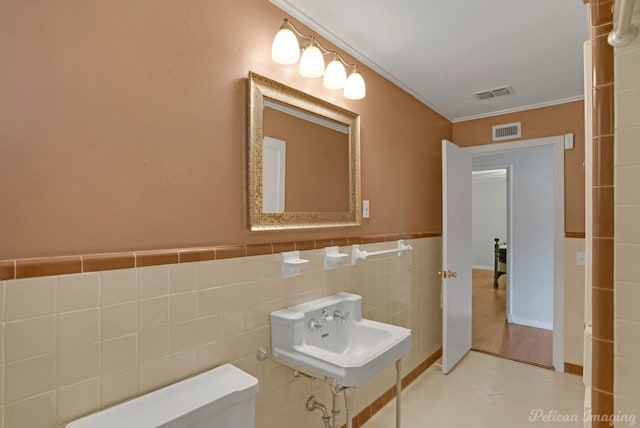 half bath featuring toilet, tile walls, crown molding, a sink, and a wainscoted wall