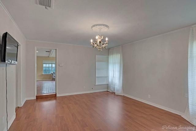 spare room featuring a chandelier, wood finished floors, ornamental molding, and baseboards