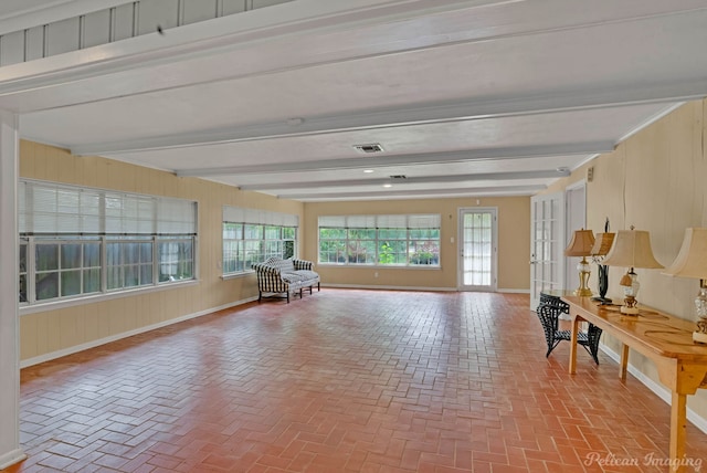 living area featuring beam ceiling, brick flooring, baseboards, and wood walls