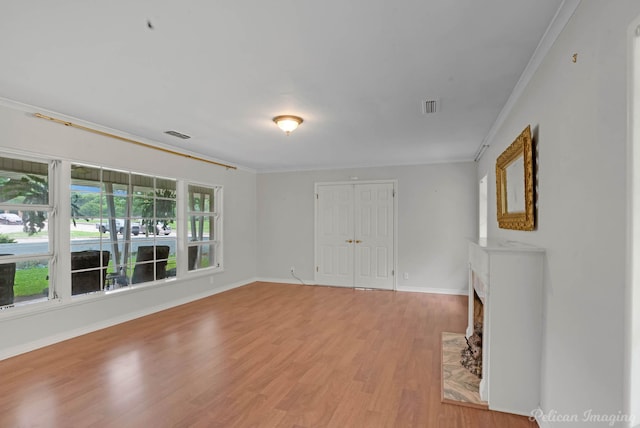 empty room featuring ornamental molding, light wood-type flooring, baseboards, and a fireplace with flush hearth