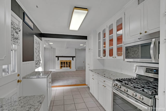 kitchen with stainless steel appliances, white cabinetry, glass insert cabinets, a wainscoted wall, and beamed ceiling