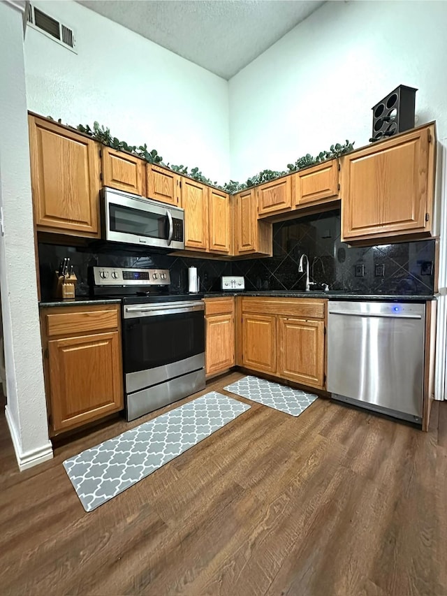 7568 Casburn Ct, Fort Worth, TX 76120 - kitchen with stainless steel appliances, dark wood-type flooring, dark countertops, a sink, and decorative backsplash