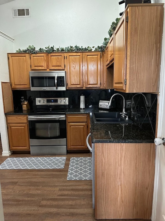 7568 Casburn Ct, Fort Worth, TX 76120 - kitchen with stainless steel appliances, a sink, dark wood-style floors, decorative backsplash, and brown cabinets