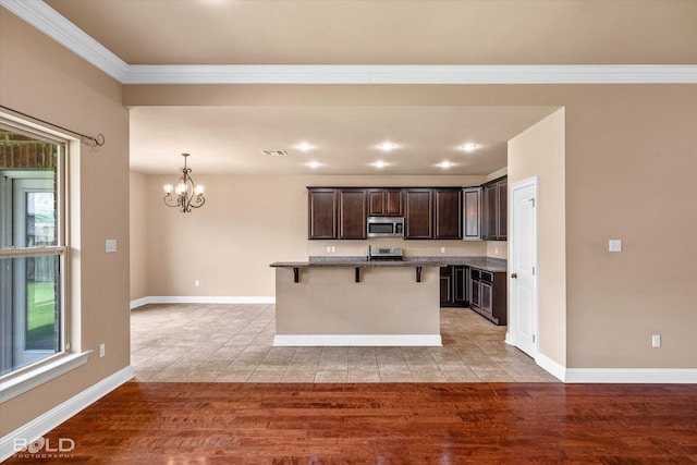 9214 Mykanos Trl, Shreveport, LA 71106 - kitchen with stainless steel microwave, a chandelier, a breakfast bar, dark brown cabinets, and light wood-style flooring