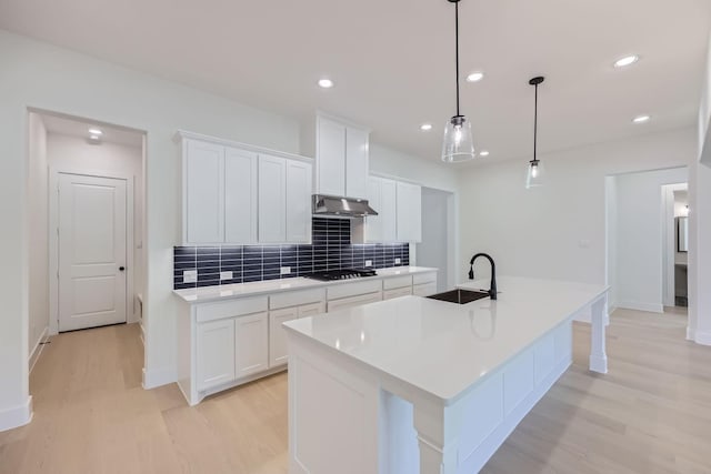 180 Shoreview Dr, Rhome, TX 76078 - kitchen featuring a sink, under cabinet range hood, light wood finished floors, decorative backsplash, and a kitchen island with sink