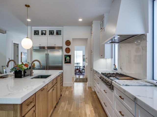 5019 Lark Ln, Dallas, TX 75209 - kitchen with stainless steel appliances, wall chimney exhaust hood, light wood finished floors, an island with sink, and glass insert cabinets