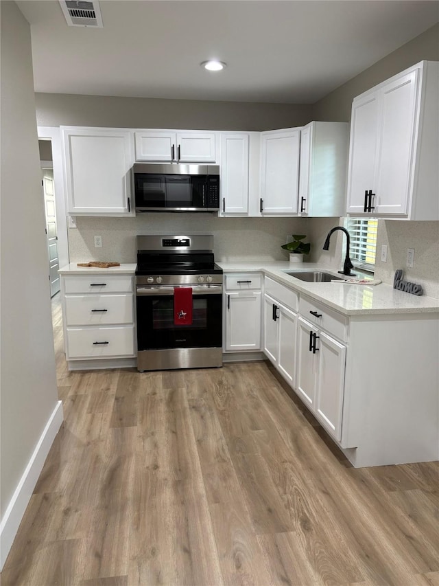3214 51st St, Dallas, TX 75216 - kitchen featuring appliances with stainless steel finishes, a sink, light wood-style floors, white cabinets, and recessed lighting