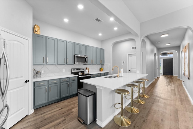 1412 Inks Dr, Desoto, TX 75115 - kitchen featuring appliances with stainless steel finishes, a sink, arched walkways, wood finished floors, and a breakfast bar area