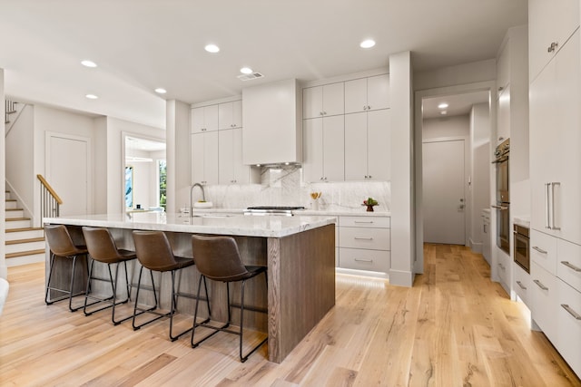 7718 Morton St, Dallas, TX 75209 - kitchen featuring a breakfast bar, a kitchen island with sink, light wood-style flooring, modern cabinets, and recessed lighting