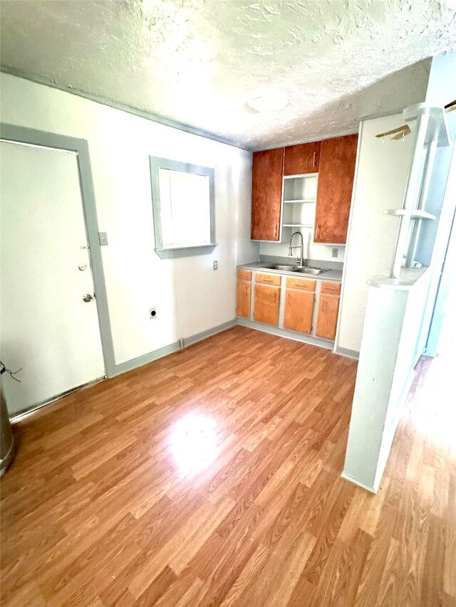 301 Beckham St E, Sulphur Springs, TX 75482 - kitchen featuring a sink, light wood-style flooring, a textured ceiling, brown cabinetry, and open shelves
