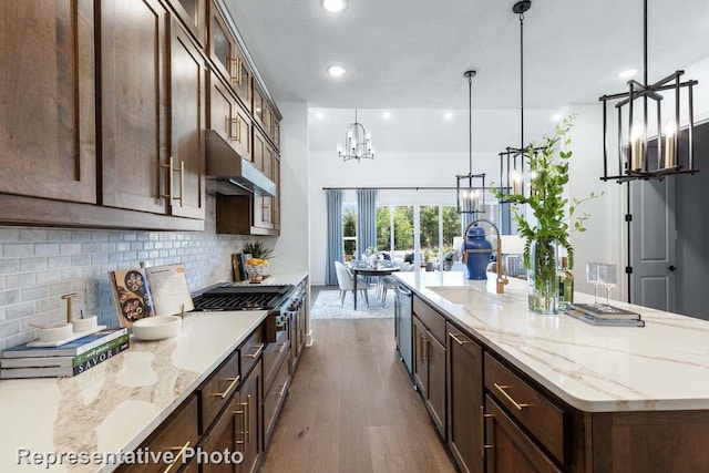2408 Plumeria Ln, Celina, TX 75009 - kitchen with under cabinet range hood, a sink, dark wood-style flooring, a chandelier, and decorative backsplash
