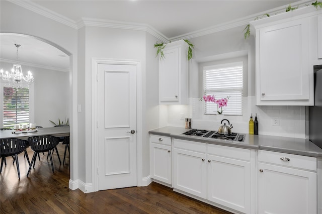 kitchen with stainless steel gas cooktop, dark wood-style flooring, arched walkways, decorative backsplash, and a chandelier