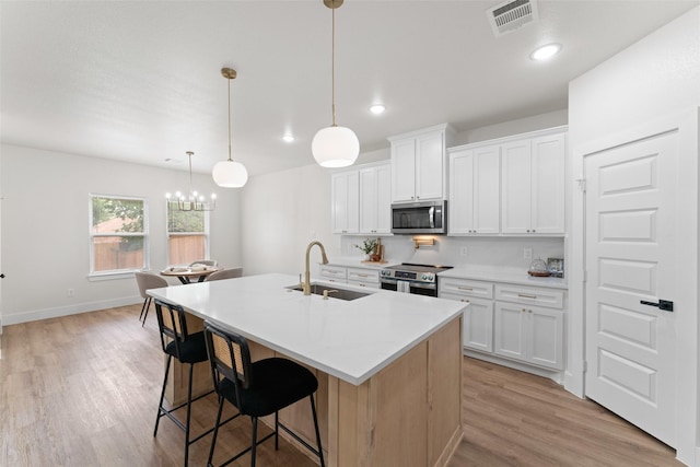 2104 Danner St, Fort Worth, TX 76105 - kitchen with stainless steel appliances, a sink, light wood-style flooring, a kitchen island with sink, and a kitchen breakfast bar
