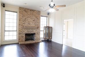 2305 Meadowlark Ln, Bedford, TX 76021 - unfurnished living room featuring dark wood-style flooring, a ceiling fan, a brick fireplace, and a decorative wall