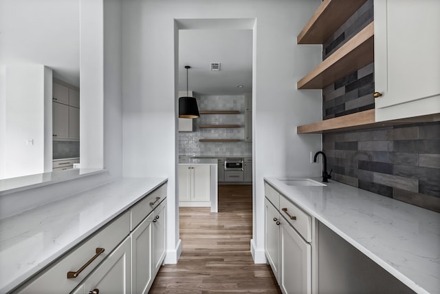 9234 San Fernando Way, Dallas, TX 75218 - kitchen with open shelves, a sink, tasteful backsplash, light stone counters, and dark wood-style floors