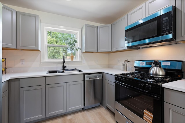 1006 Irene Dr, Mesquite, TX 75149 - kitchen with appliances with stainless steel finishes, gray cabinetry, a sink, light countertops, and light wood finished floors