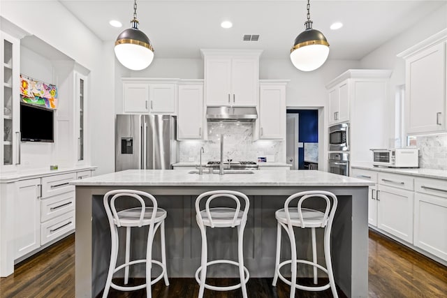 2237 Gatsby Way, Carrollton, TX 75010 - kitchen with appliances with stainless steel finishes, under cabinet range hood, white cabinetry, an island with sink, and decorative backsplash