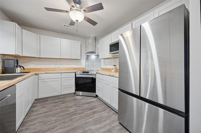 563 Country Club Rd, Bowie, TX 76230 - kitchen featuring appliances with stainless steel finishes, butcher block countertops, wall chimney range hood, ceiling fan, and light wood finished floors