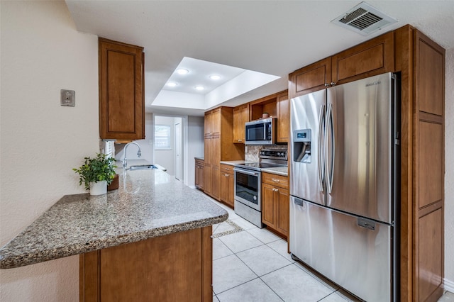 5072 Stanley Dr, The Colony, TX 75056 - kitchen featuring stainless steel appliances, a sink, a tray ceiling, brown cabinetry, and recessed lighting