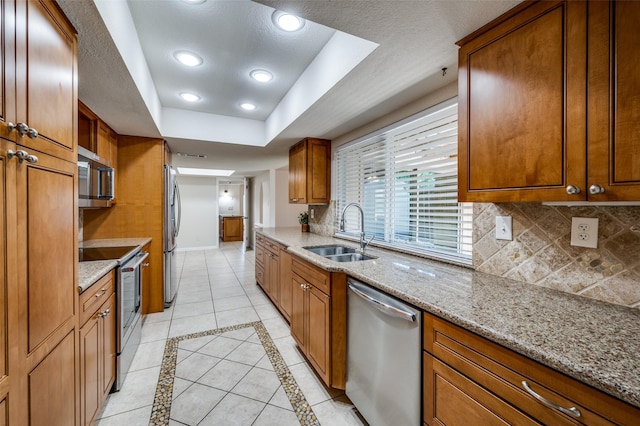 5072 Stanley Dr, The Colony, TX 75056 - kitchen featuring stainless steel appliances, a sink, brown cabinetry, decorative backsplash, and recessed lighting
