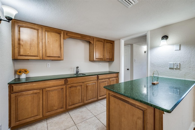 5072 Stanley Dr, The Colony, TX 75056 - kitchen featuring a sink, brown cabinetry, light tile patterned flooring, a textured ceiling, and a textured wall