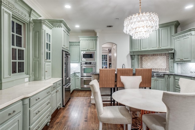 kitchen with appliances with stainless steel finishes, arched walkways, backsplash, dark wood-style floors, and crown molding