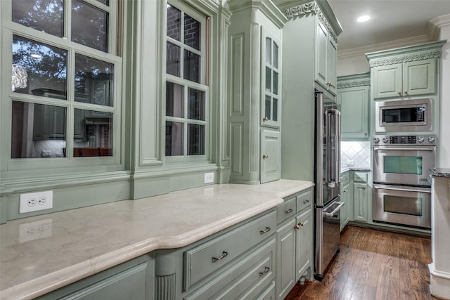kitchen featuring stainless steel appliances, dark wood finished floors, crown molding, green cabinetry, and light stone counters