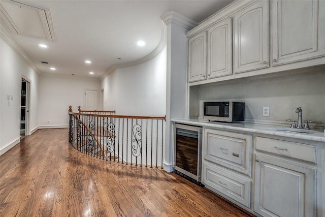 bar with beverage cooler, a sink, stainless steel microwave, crown molding, and baseboards