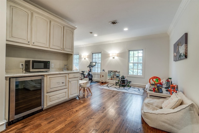 kitchen featuring wine cooler, cream cabinetry, stainless steel microwave, dark wood-type flooring, and crown molding