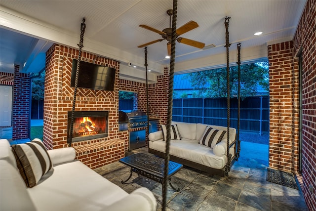 living room featuring brick wall, ceiling fan, an outdoor brick fireplace, and stone finish flooring
