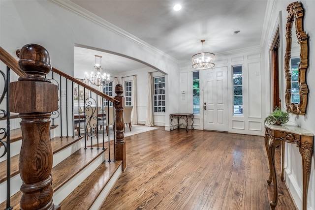 entrance foyer with a chandelier, wood finished floors, stairs, arched walkways, and crown molding