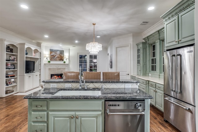 kitchen featuring high quality fridge, green cabinets, a sink, ornamental molding, and a glass covered fireplace