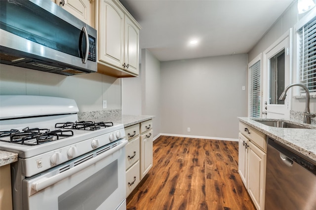 2018 Shawnee St, Denton, TX 76209 - kitchen featuring appliances with stainless steel finishes, a sink, dark wood-style flooring, light stone countertops, and baseboards