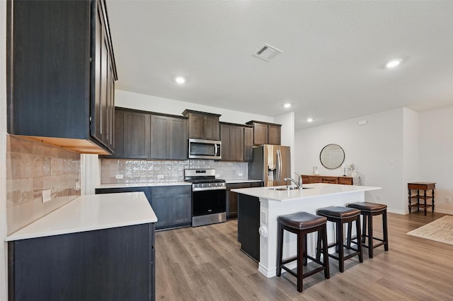 312 Duke Ct, Fate, TX 75189 - kitchen featuring appliances with stainless steel finishes, a kitchen breakfast bar, a sink, light wood-style floors, and tasteful backsplash