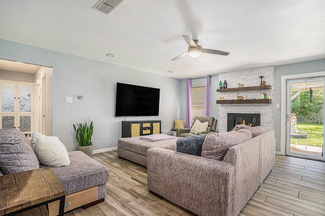 629 Barbara Ln, Burleson, TX 76028 - living room featuring a ceiling fan, light wood-type flooring, a stone fireplace, a textured ceiling, and baseboards
