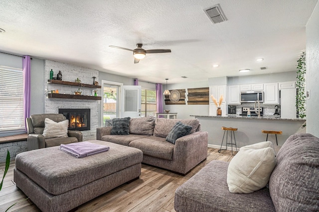 629 Barbara Ln, Burleson, TX 76028 - living area with light wood-style flooring, a ceiling fan, a textured ceiling, and a fireplace