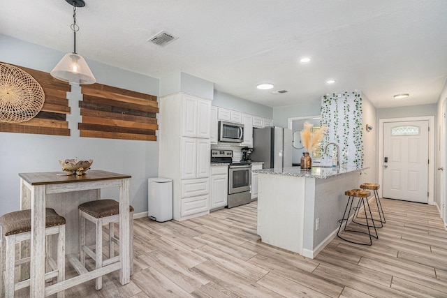 629 Barbara Ln, Burleson, TX 76028 - kitchen with stainless steel appliances, a kitchen bar, light wood-type flooring, white cabinets, and baseboards
