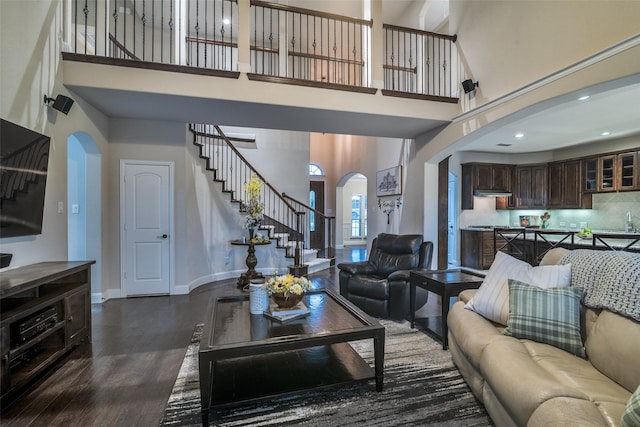 611 Southwestern Dr, Rockwall, TX 75087 - living room featuring arched walkways, a towering ceiling, stairs, dark wood-style flooring, and baseboards