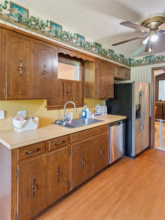 kitchen featuring stainless steel dishwasher, a sink, light wood-style floors, a textured ceiling, and light countertops
