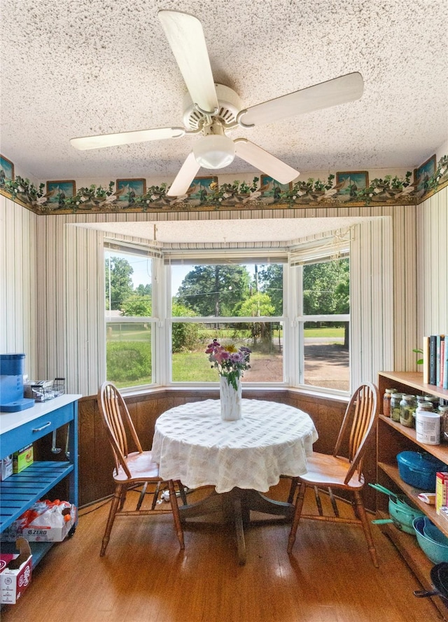 dining space featuring wood finished floors, a textured ceiling, and a ceiling fan