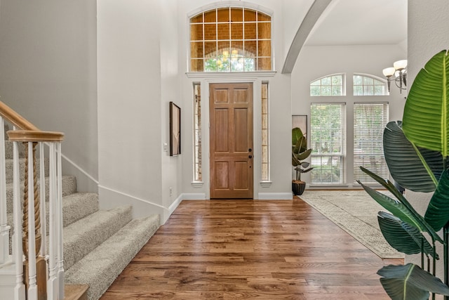 entrance foyer with a chandelier, wood finished floors, stairway, arched walkways, and a high ceiling