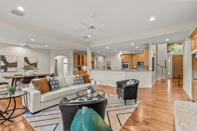 living area with ceiling fan, arched walkways, light wood finished floors, recessed lighting, and ornamental molding