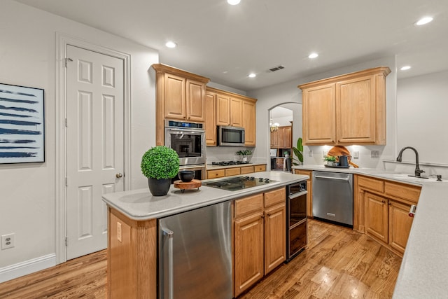 kitchen with appliances with stainless steel finishes, a sink, arched walkways, light countertops, and light wood finished floors