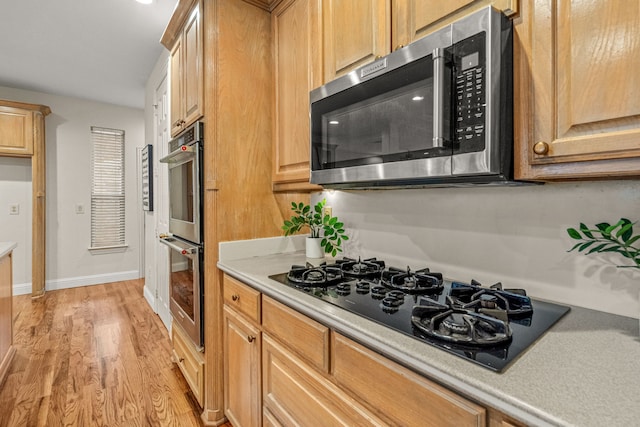 kitchen featuring appliances with stainless steel finishes, light wood-type flooring, light countertops, and baseboards
